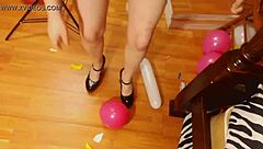 Fifi Foxx playfully pops colorful balloons while strutting in shiny high heels for fun.